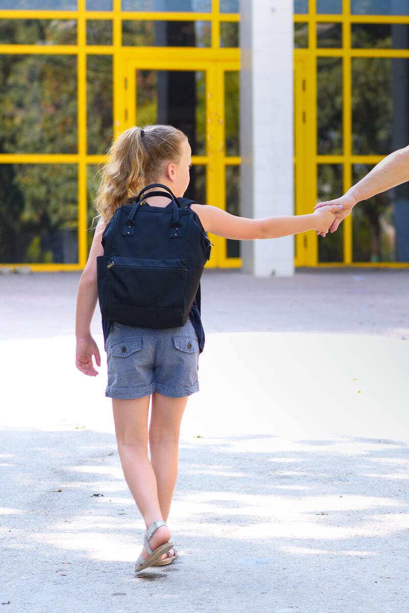 Young girl walking to school and holding hands with parent