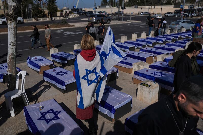 People stand by coffins covered with Israeli flags that are meant to symbolise the price Israel will pay for agreeing to a ceasefire with Hamas (Ohad Zwigenberg/AP)