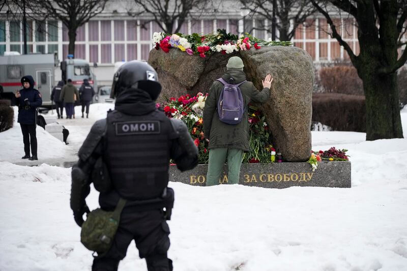 A police officer watches as a man lays flowers at the monument where the first camp of the Gulag political prison system was established, in St Petersburg (Dmitri Lovetsky/AP)