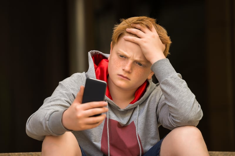 A boy with ginger hair feeling stressed while looking at his phone