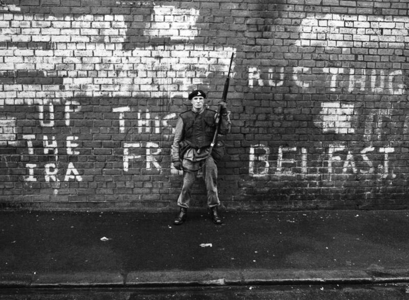 An armed British soldier on patrol in Belfast in 1971, standing against a wall with graffiti