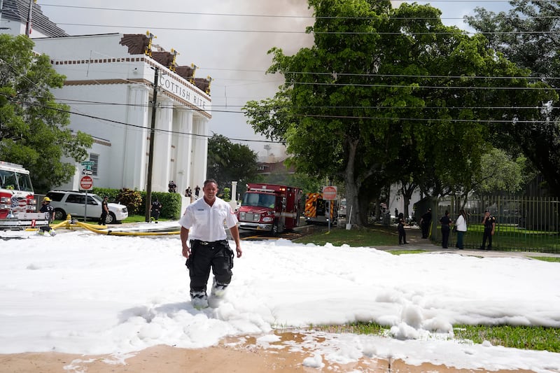 A firefighter walks from the scene of the blaze with foam across the ground (Lynne Sladky/AP)