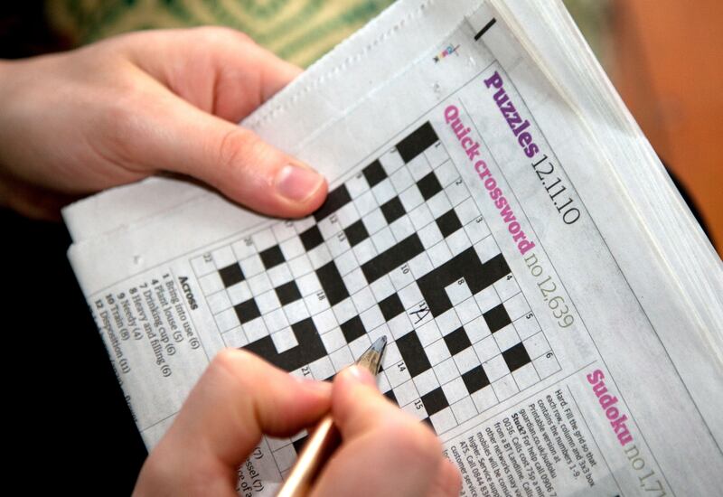 Picture of a woman filling in answers to a crossword in a newspaper