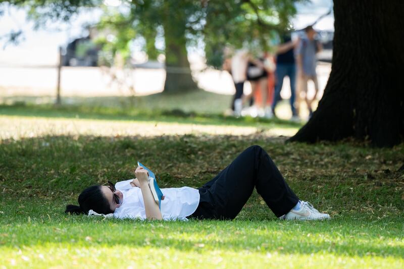 A person reads a book in Hyde Park, London, during recent warm weather