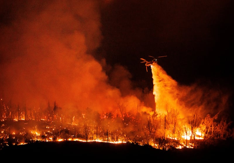 A night-flying helicopter drops water on flames as the Thompson Fire continues to burn (AP Photo/Ethan Swope)