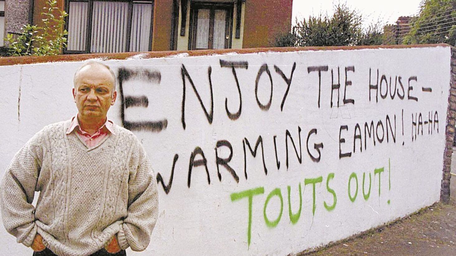 Former IRA man Eamon Collins beside graffiti which appeared in Newry after his home had been set on fire. Picture by Cathal McNaughton 