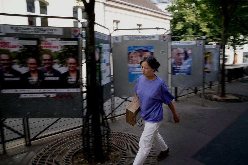 A woman walks past campaign boards for the forthcoming parliamentary elections in Paris (Christophe Ena/AP)