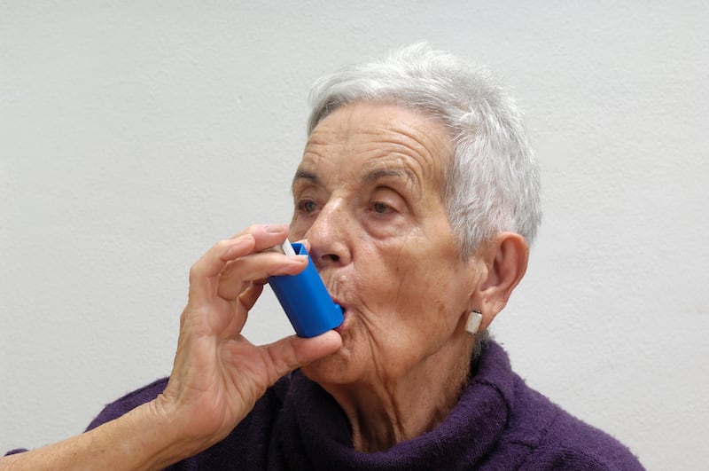 Old woman with short grey hair using an inhaler