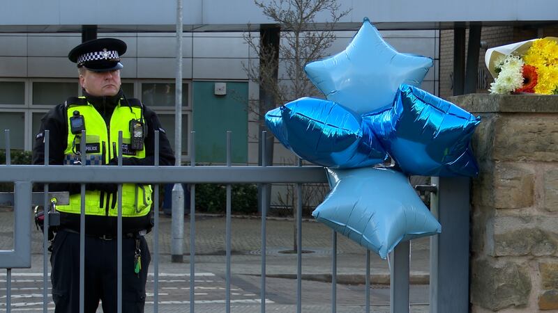 A police officer stands next to floral tributes left outside All Saints Catholic High School