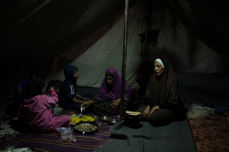 Randa Baker, right, and her family, who were displaced by the Israeli bombardment of the Gaza Strip, break their fast on the first day of Ramadan at a makeshift tent camp in Muwasi (Fatima Shbair/AP)
