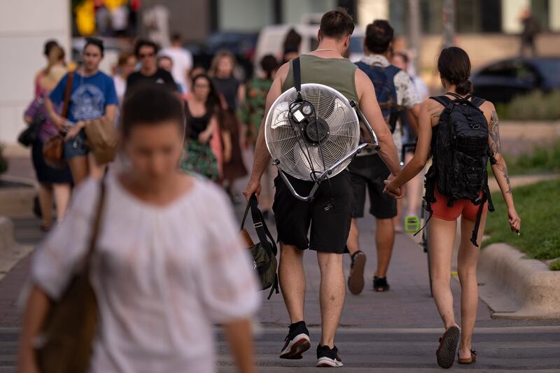 A woman walks holding hands with a man carrying an electric fan on his back on a hot evening in Bucharest, Romania (AP)