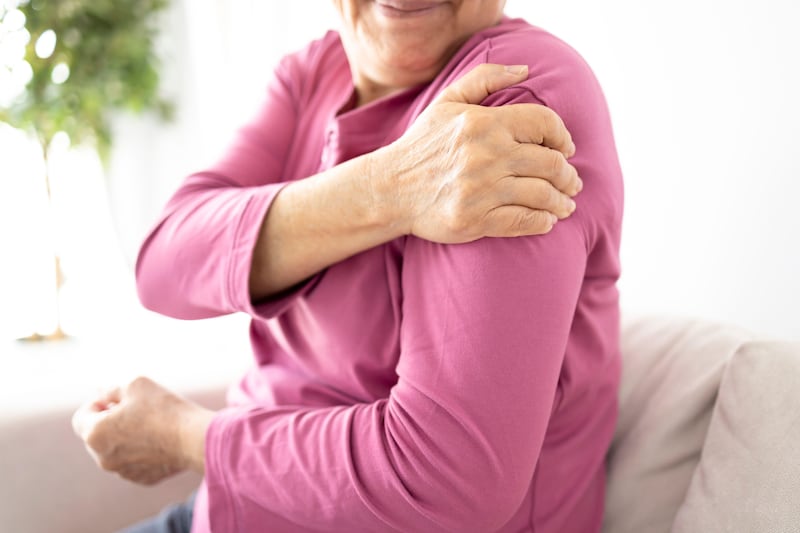 A senior woman wearing a pink top clutching at her shoulder.