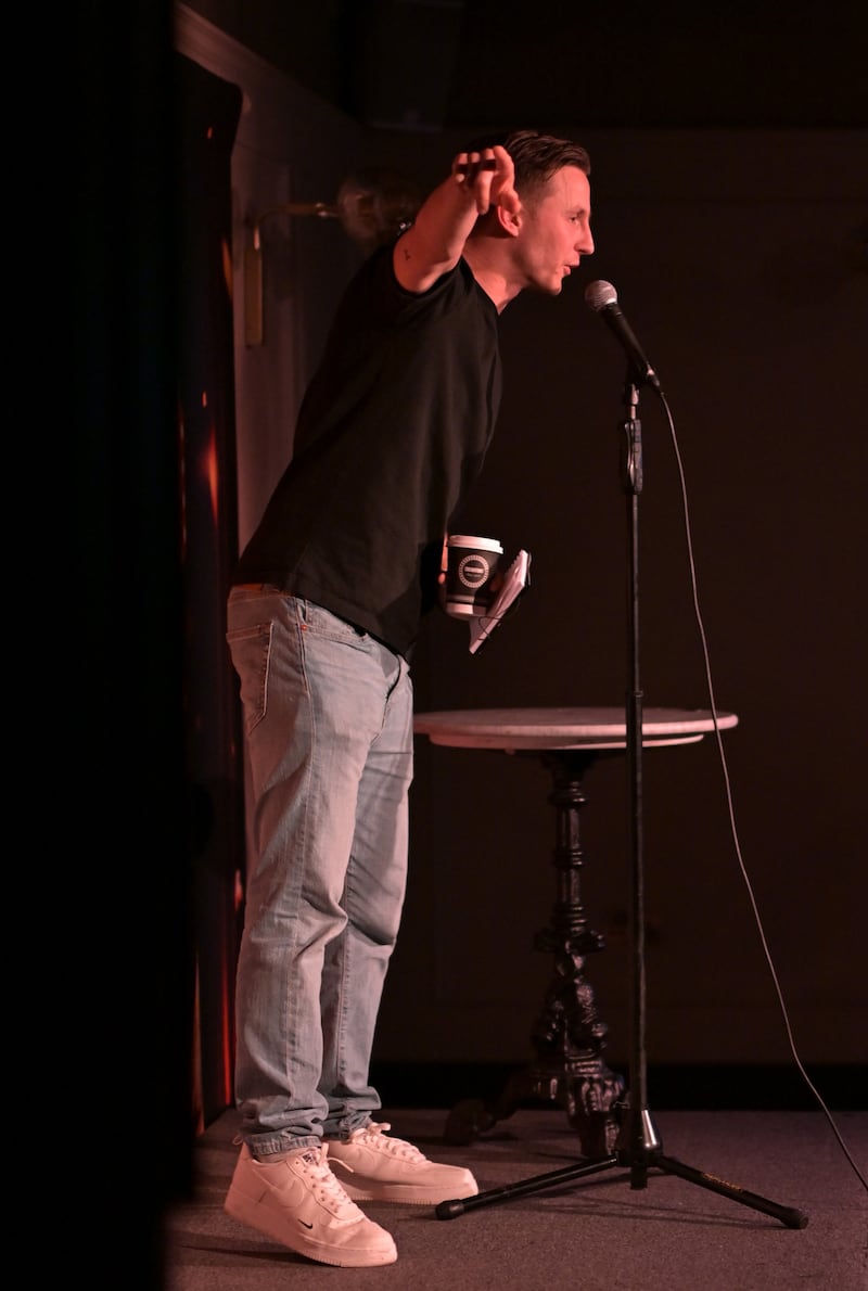 Male stand-up comedian gestures on stage while holding microphone