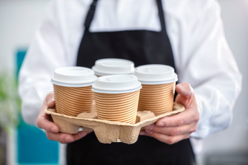 Waiter barista holding and serving take out a paper disposable cup of hot coffee in cafe.