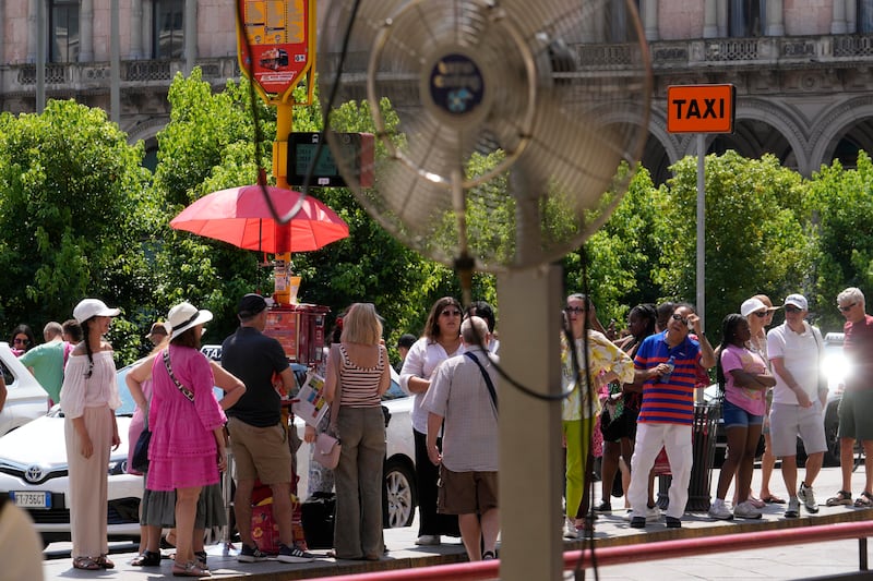 Tourists try to find some shade as they wait for a bus in Milan (Luca Bruno/AP)