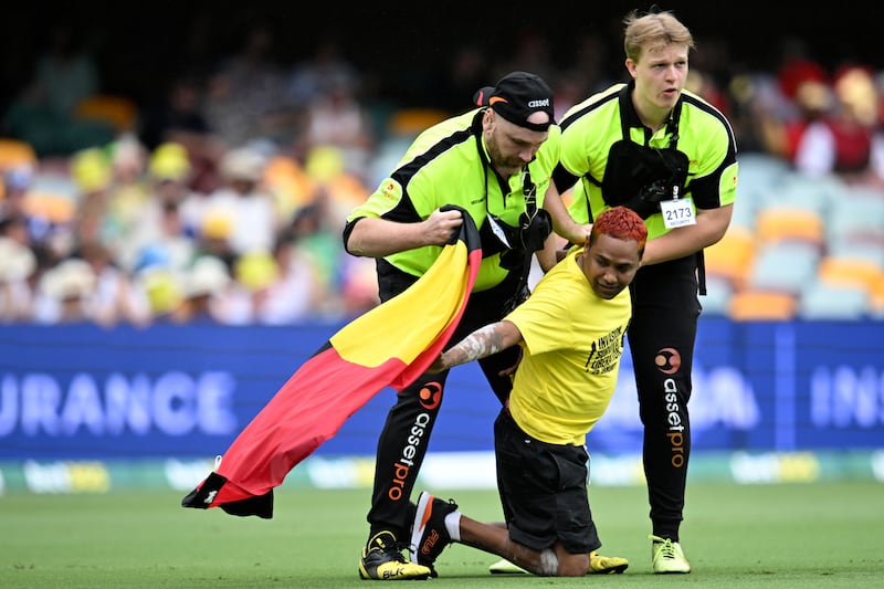 A protester carrying an Aboriginal flag is apprehended by security on the second day of the cricket test match between Australia and the West Indies in Brisbane (Darren England/AAP/AP)