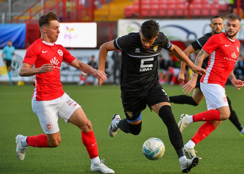 A footballer wearing a black jersey running beside a footballer in a red jersey attempting to take the ball from the player in black