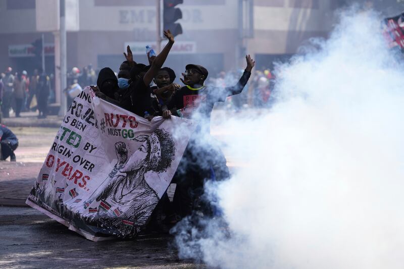 Protesters hide behind a banner as police fire tear gas at them during a protest over proposed tax hikes in a finance Bill in Nairobi, Kenya (Brian Inganga/AP)