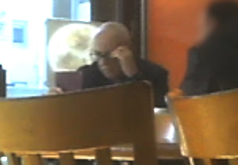 Anthony Beard sitting at a table in a cafe during a meeting with one of his clients, holding a passport.