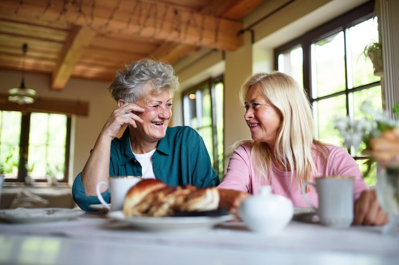 Two senior women chatting and having coffee and cake at home