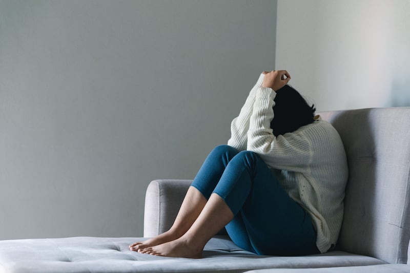 Sad teenage girl hunched up on a sofa covering her face