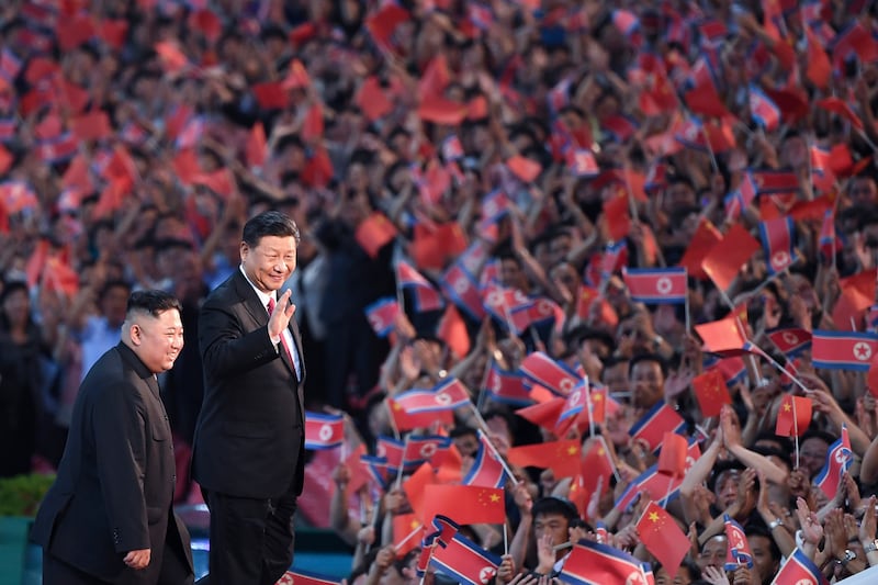 Spectators wave Chinese and North Korean flags as North Korean leader Kim Jong Un, left, and visiting Chinese President Xi Jinping attend a mass gymnastic performance in 2019 (Yan Yan/Xinhua via AP, File)