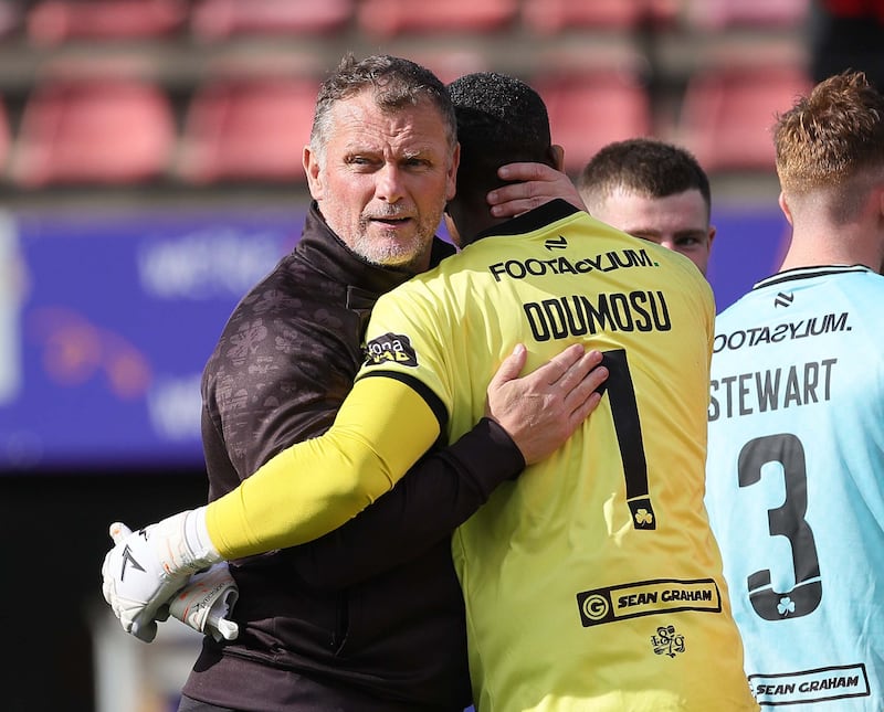 A man in a black jacket hugging a man in a yellow football kit