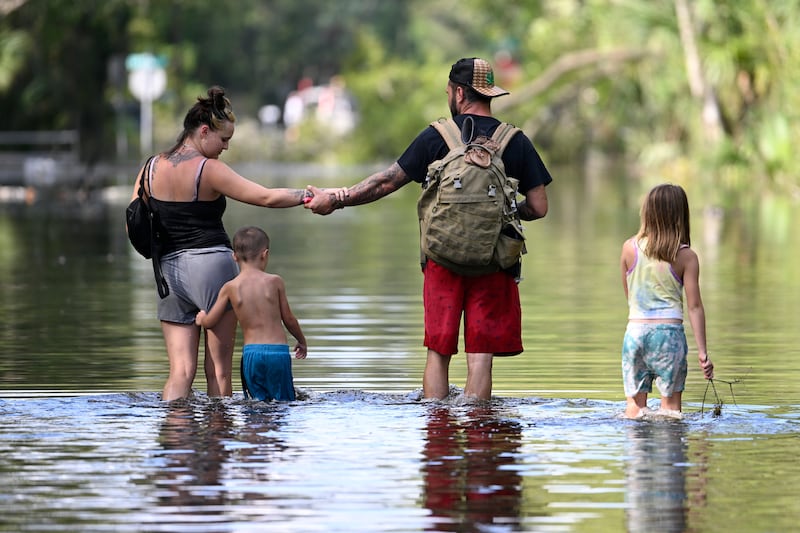 Dustin Holmes, second from right, holds hands with his girlfriend, Hailey Morgan, while returning to their flooded home with her children Aria Skye Hall, 7, right, and Kyle Ross, 4, in Crystal River, Florida (Phelan M Ebenhack/AP)