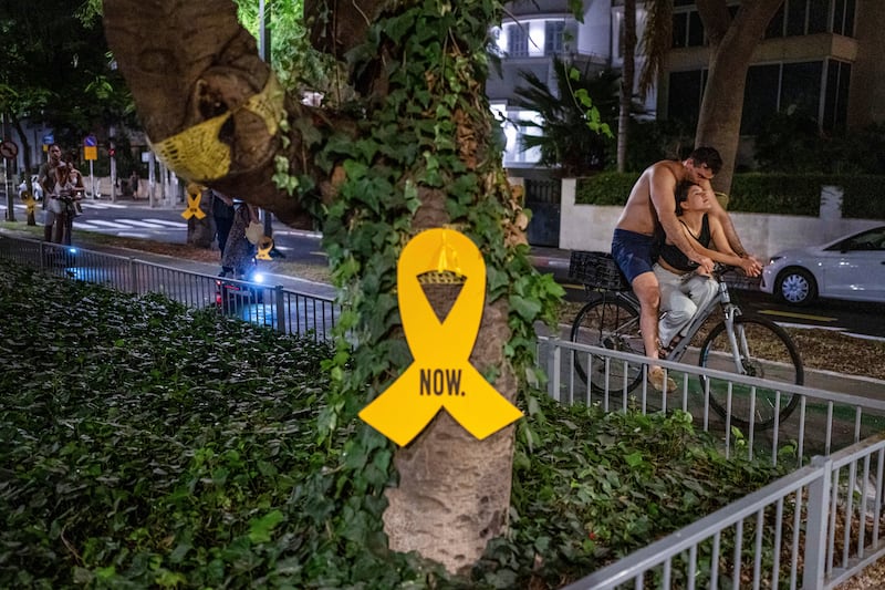 A couple rides a bicycle near a yellow ribbon sign calling for the release of hostages (AP Photo/Ohad Zwigenberg)