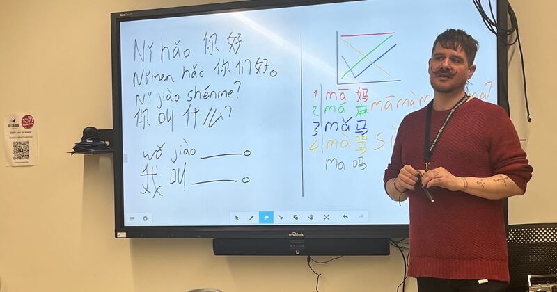 A picture of Pól Ó Néill teaching Chinese through the medium of Irish in front of a whiteboard in Raidió Fáilte