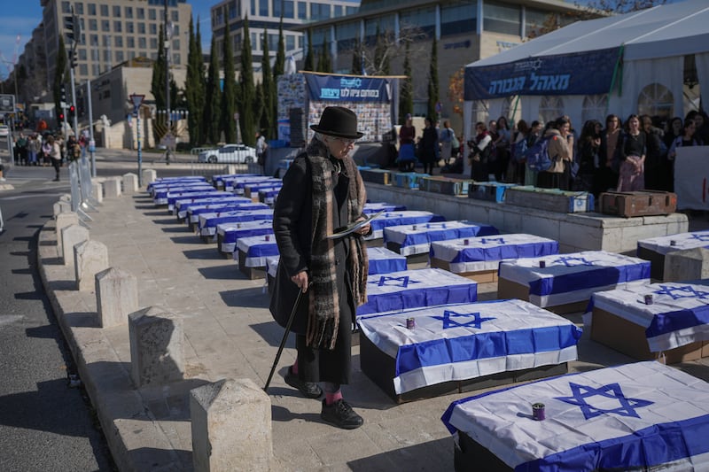 A woman walks by mock coffins in Jerusalem covered with Israeli flags that are meant to symbolise the price Israel will pay for agreeing to a ceasefire with Hamas (Ohad Zwigenberg/AP)