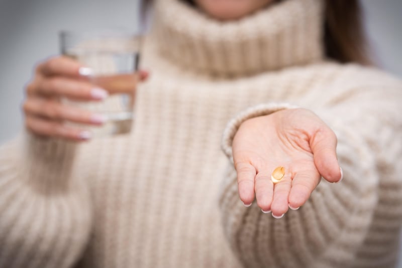 A woman holding a Vitamin D tablet and a glass of water