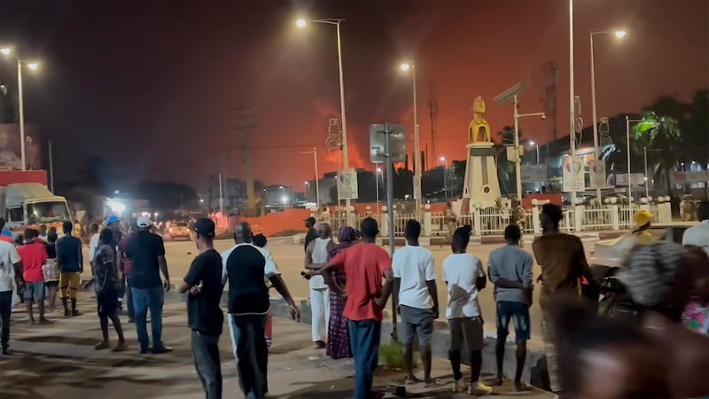 Residents watch a plume of smoke from a burning oil depot in Conakry, Guinea, on Monday (AP)