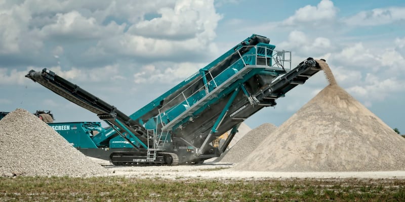 A large green Powerscreen machine operating in a quarry site.