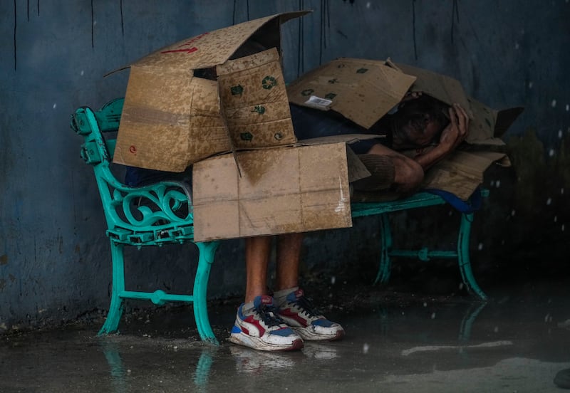 People at a bus stop shield themselves with cardboard amid wind and rain during the passage of Hurricane Rafael in Havana (Ramon Espinosa/AP)