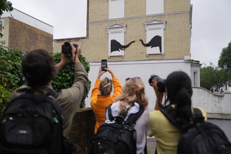 People photograph the Banksy depicting two elephants poking their heads out of blocked out windows