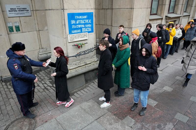 A police officer checks voters queueing at a polling station in St Petersburg, Russia, at noon on Sunday (Dmitri Lovetsky/AP)