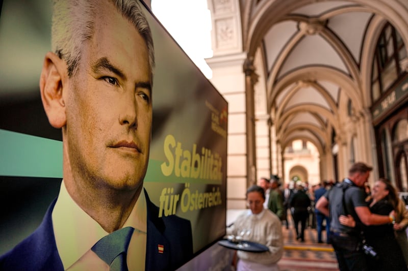 People gather next to a poster of Austrian chancellor Karl Nehammer at the OVP, Austrian People’s Party, headquarters in Vienna (AP Photo/Andreea Alexandru)