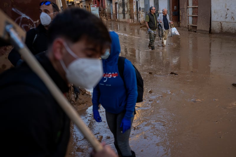 Residents walk over a muddy street as volunteers work in Massanassa, Valencia (Emilio Morenatti/AP)