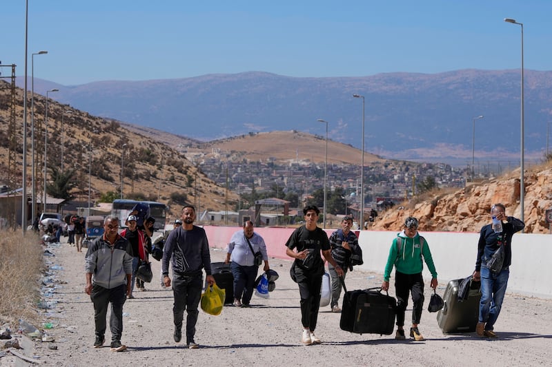 People carry their luggage as they cross into Syria on foot (Hassan Ammar/AP)