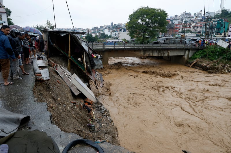 People gather at the edge of the Bagmati River in spate after heavy rains in Kathmandu (Gopen Rai/AP)