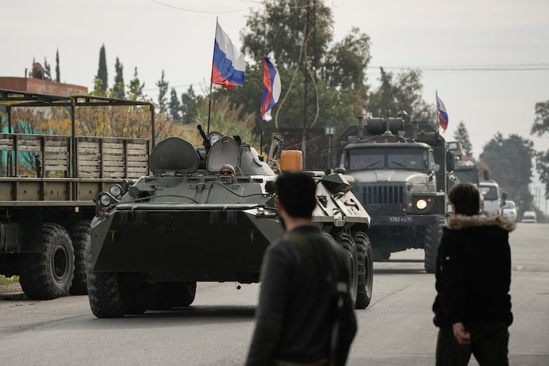 Syrian fighters watch Russian armoured vehicles driving past near the Hmeimim Air Base (Leo Correa/AP)