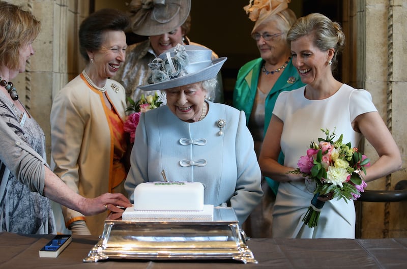 The then-Countess of Wessex and the Princess Royal look on as the Queen cuts a Women’s Institute 100th anniversary cake in 2015