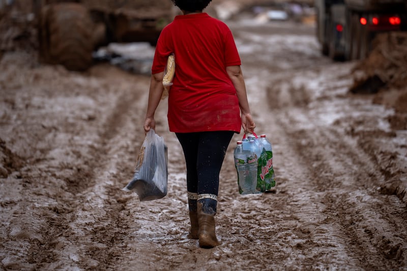 A woman carrying water and boots walks through the muddy streets after the floods in in Masanasa, Valencia, Spain (Emilio Morenatti/AP)