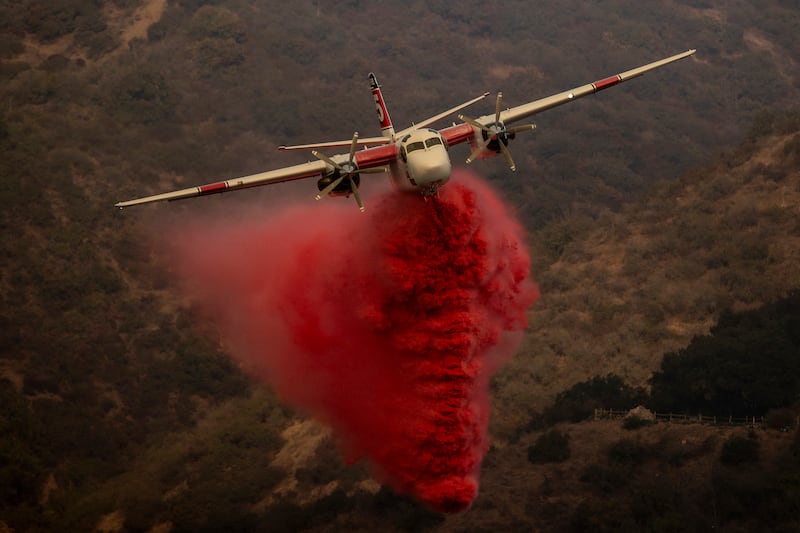 A firefighting aircraft releases retardant while battling the Palisades Fire in the Mandeville Canyon neighbourhood of Los Angeles (Stephen Lam/AP)