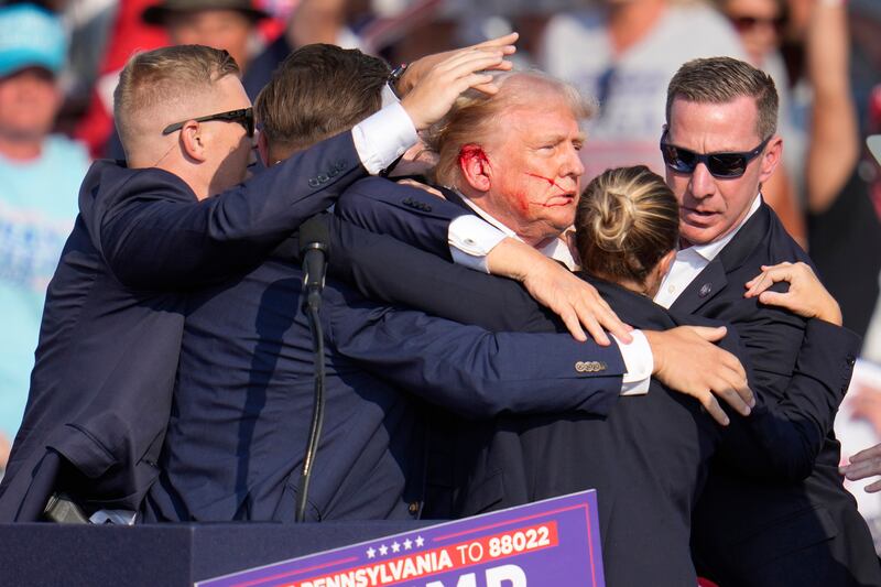 Former president Donald Trump is surrounded by US Secret Service agents as he is helped off the stage (Gene J. Puskar/AP)