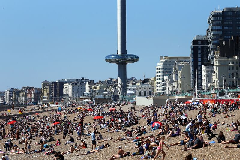 The Brighton i360 rises as people enjoy the warm weather on the beach in Brighton, East Sussex, in 2016