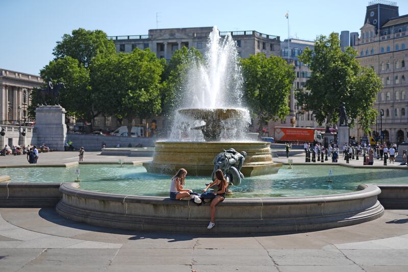 People sit by the fountains in Trafalgar Square, central London, in the sun