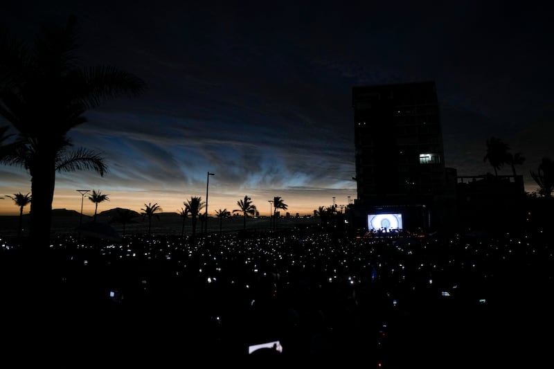 People use their mobile phones as the sky darkens in Mazatlan, Mexico (Fernando Llano/AP)