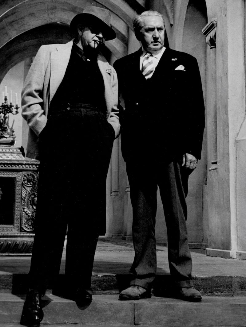 Black and white photo of two smartly dressed men standing beside each other.